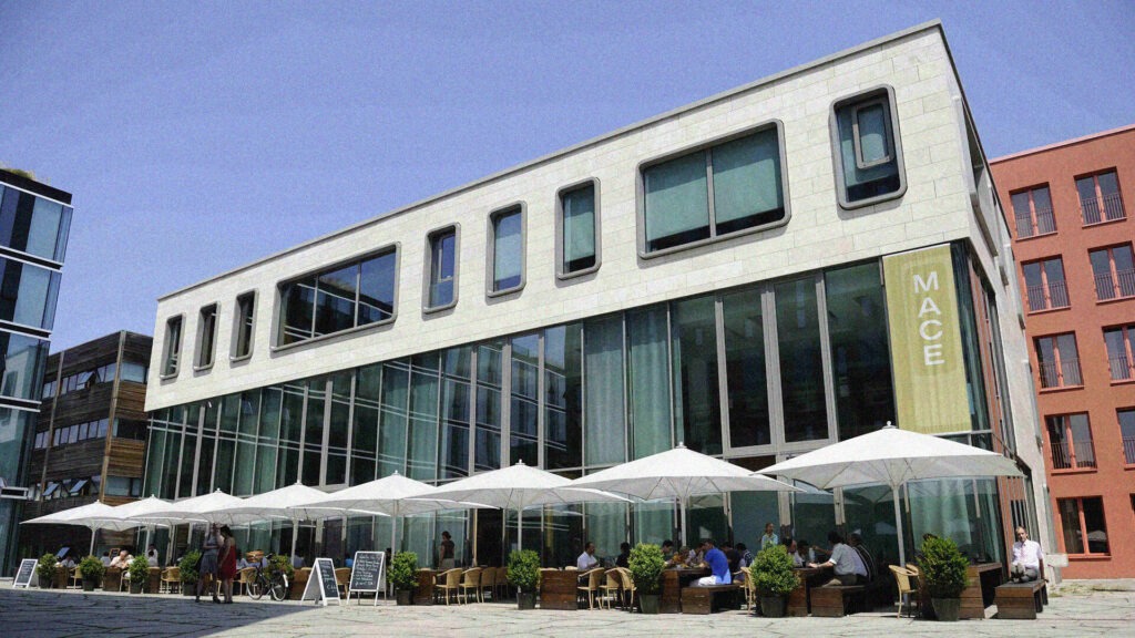 Ein großes Gebäude mit weißen Sonnenschirmen auf dem Bürgersteig unter blauem Himmel.